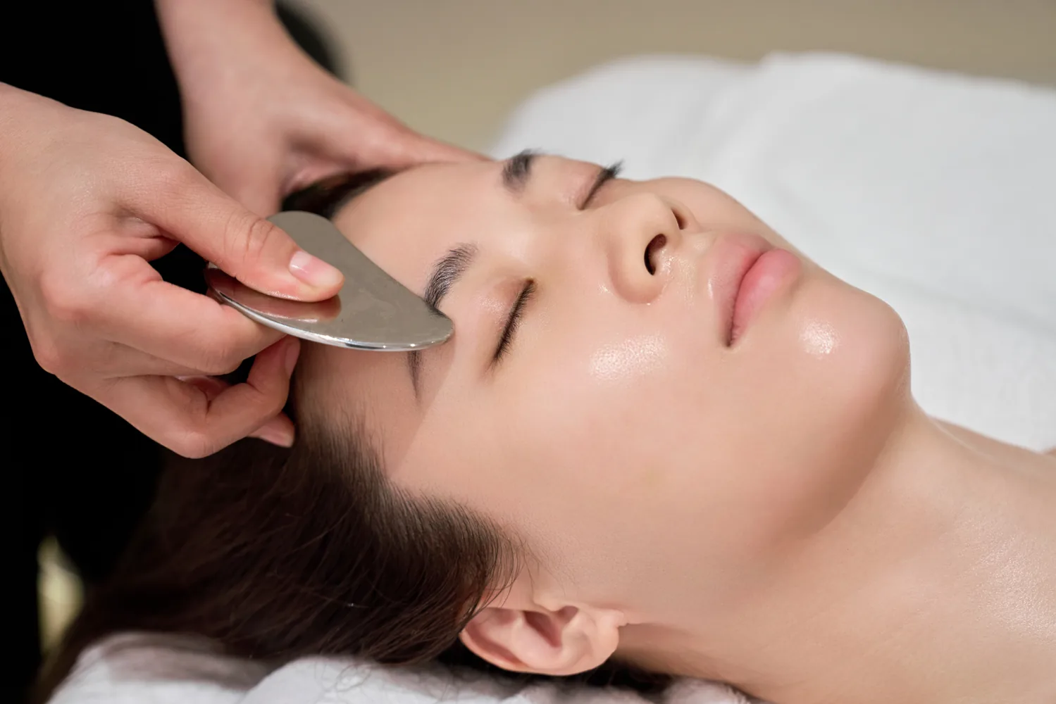 A gua sha tool used gently near the temple
